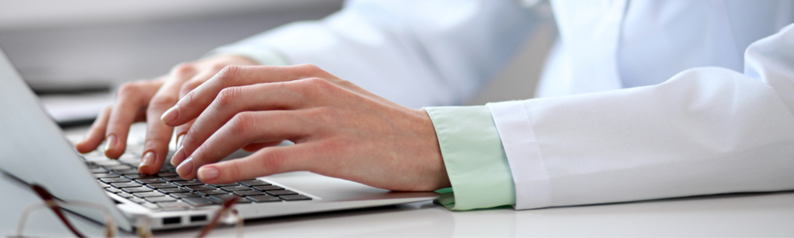 Foto con foco selectivo en manos de un médico que está digitando en el tablero frente al computador
