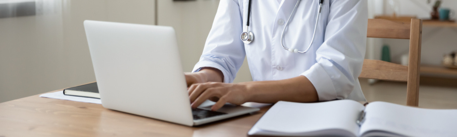 Una mujer médico sentada frente a un computador, foto enfocada en sus manos que están digitando en el teclado